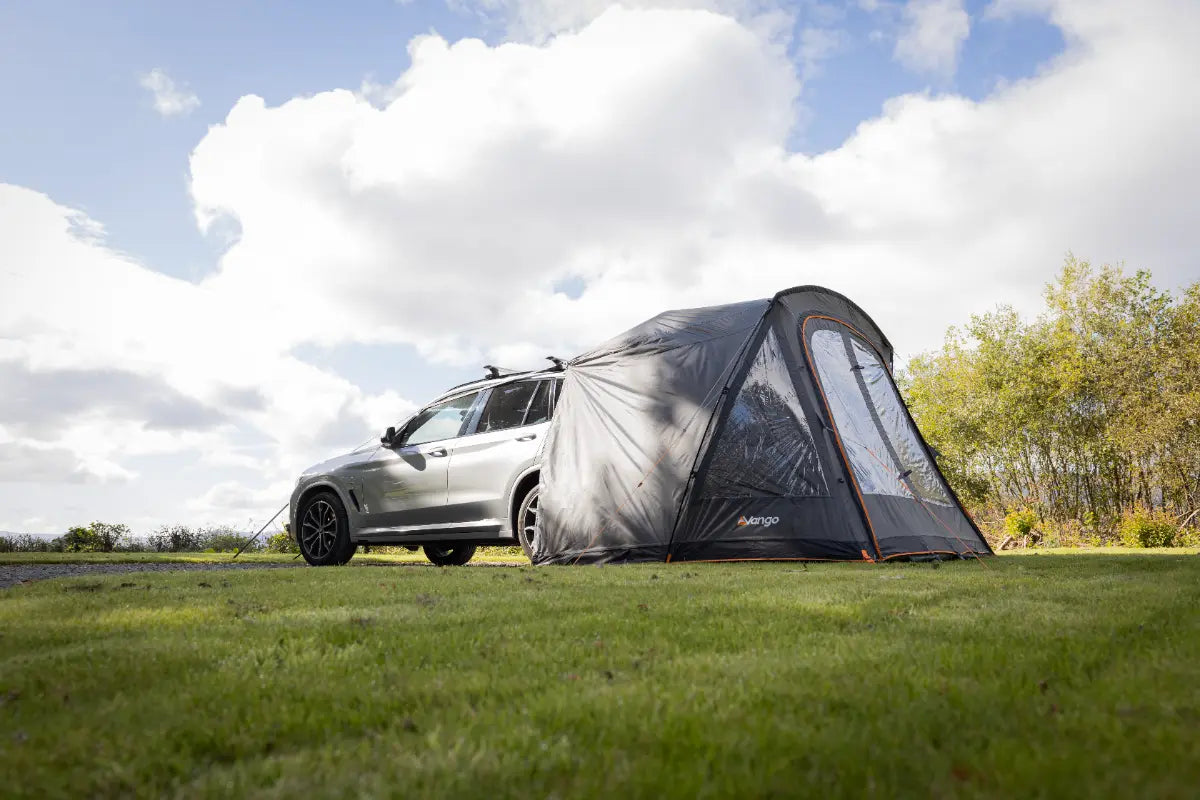 Car with an attached Vango Arden Tailgate Low Poled Awning on a grassy field under a cloudy sky.