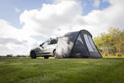 Car with an attached Vango Arden Tailgate Low Poled Awning on a grassy field under a cloudy sky.