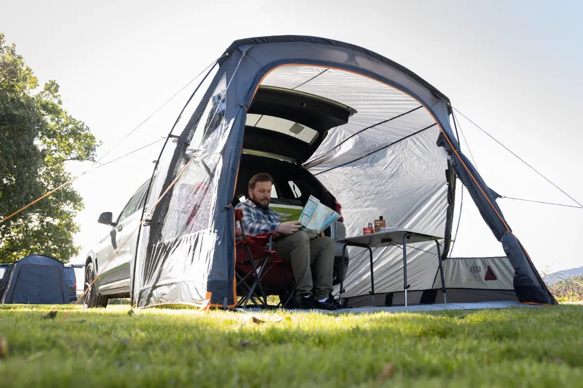 Person relaxing in the Vango Arden Tailgate Low Poled Awning, sitting on a chair.