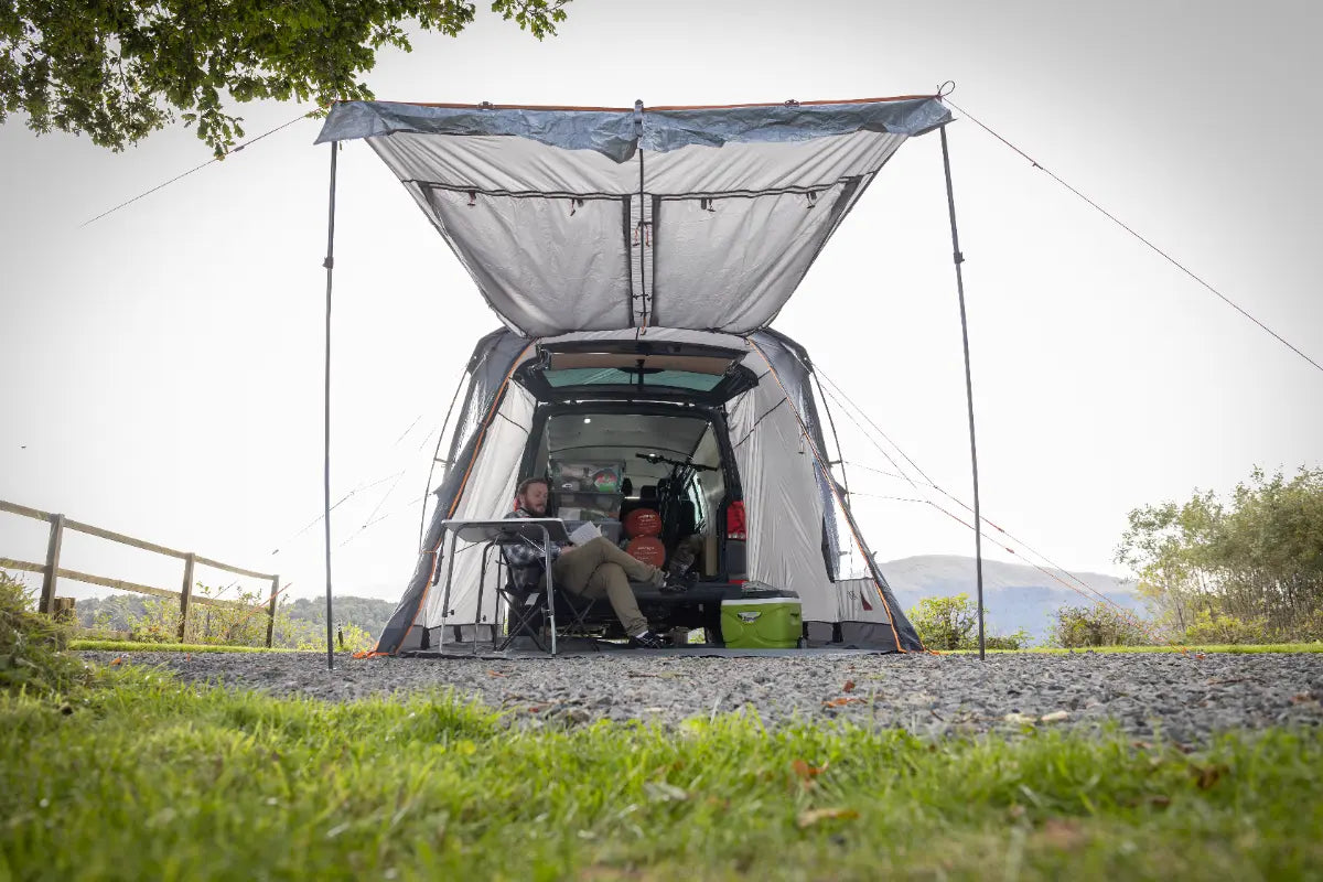 People sitting inside the Vango Arden Tailgate Low Poled Awning with grass and trees in the background.