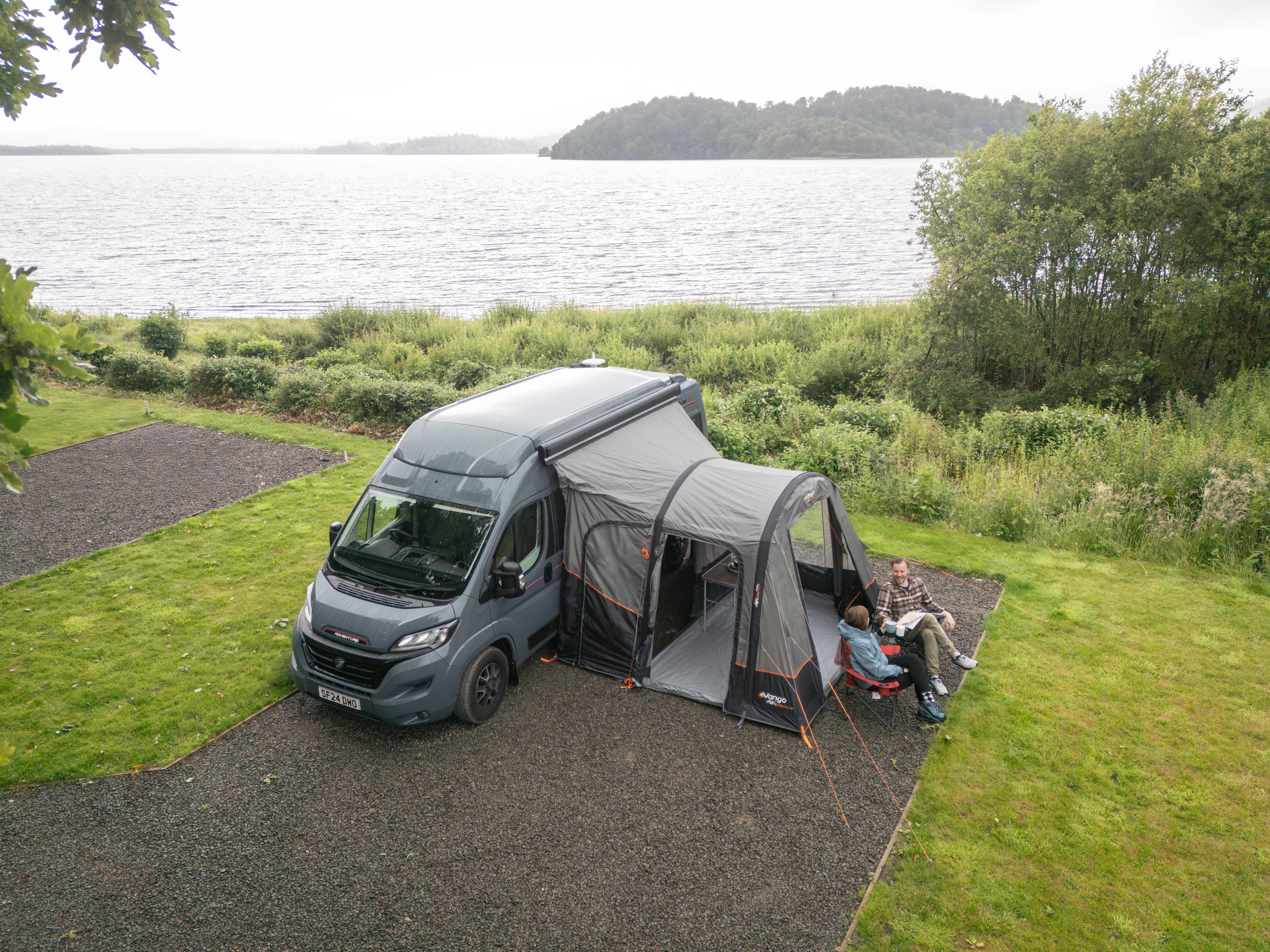 Campervan with an attached Vango Faros III Air Awning by a lake with people sitting outside