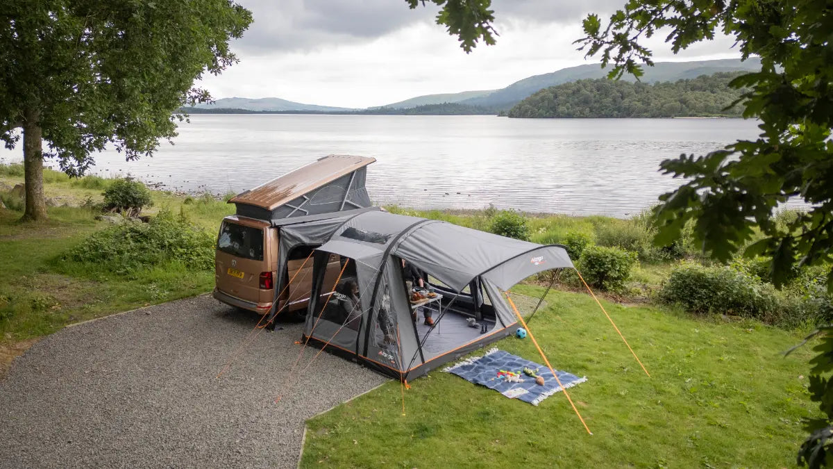 Van with Vango Kela Air Low 60th Aniversary Awning parked by a lake with mountains in the background