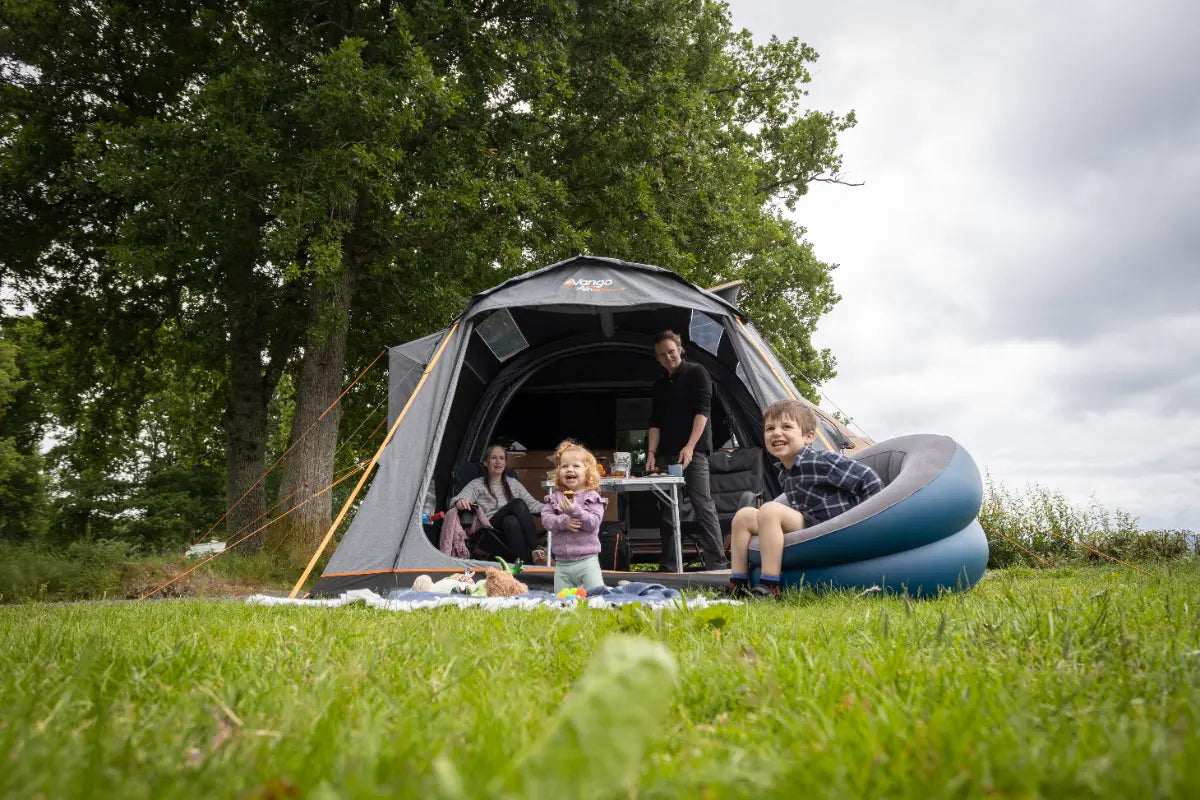 Family camping outdoors with the Vango Kela Air Low 60th Aniversary Awning on a grassy area.