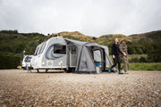 Two people standing next to a caravan with a Vango Palma Air 260 awning in a scenic outdoor setting.