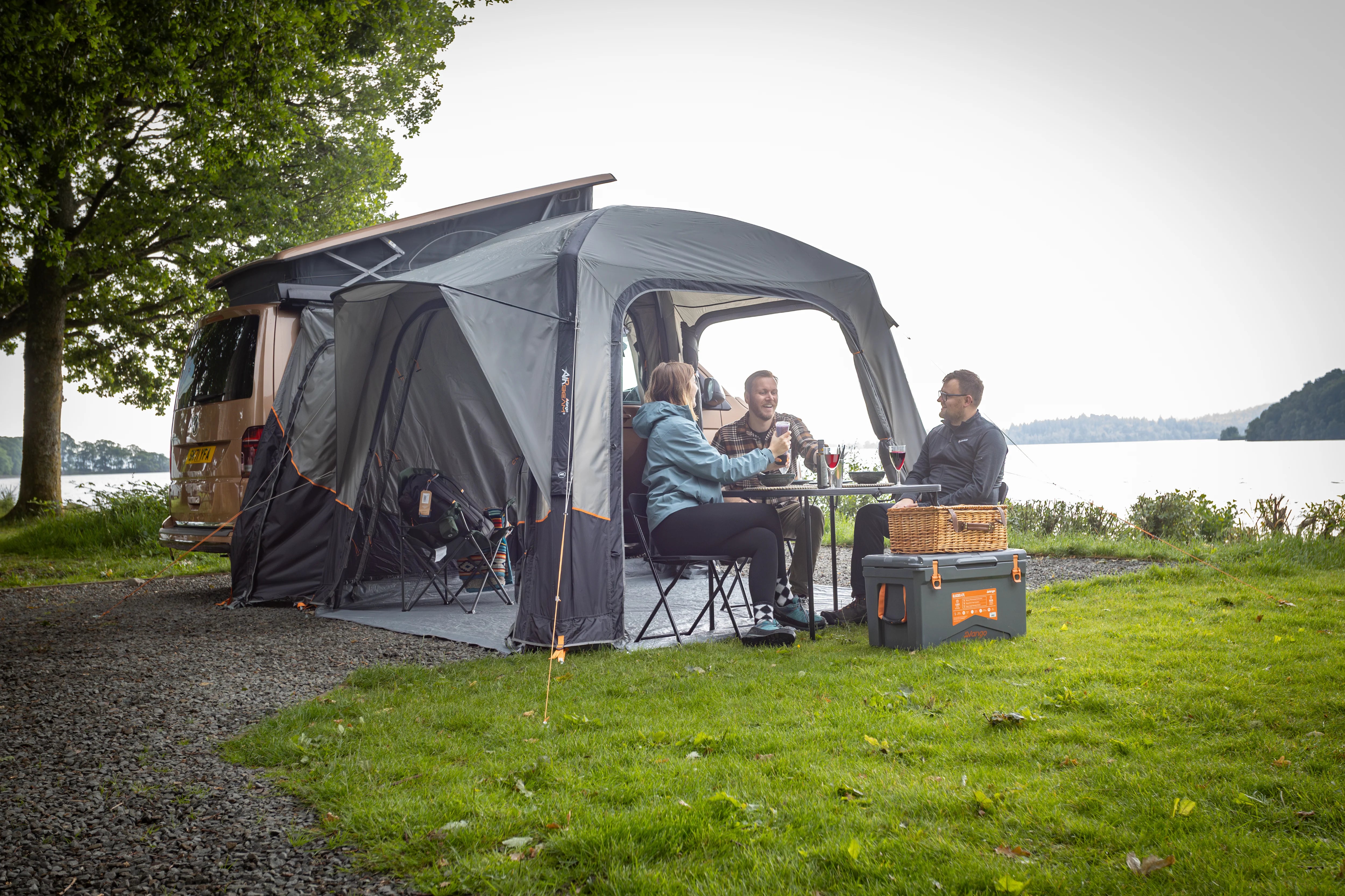 Three people spending time under the Quadris Air Low Drive Away Awning nearby a lake