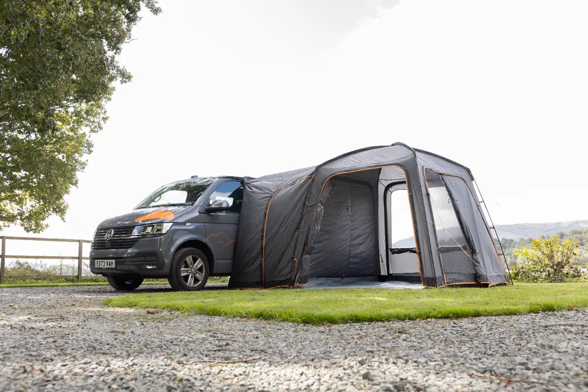Van with the Vango Tailgate Hub II Low Poled awning attached on a gravel road with greenery in the background