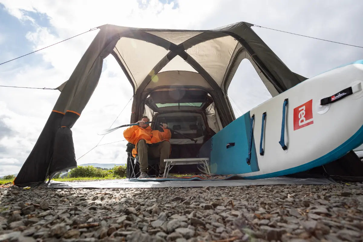Person sitting inside the Vango Tailgate Airhub II Low awning, next to a surfboard.