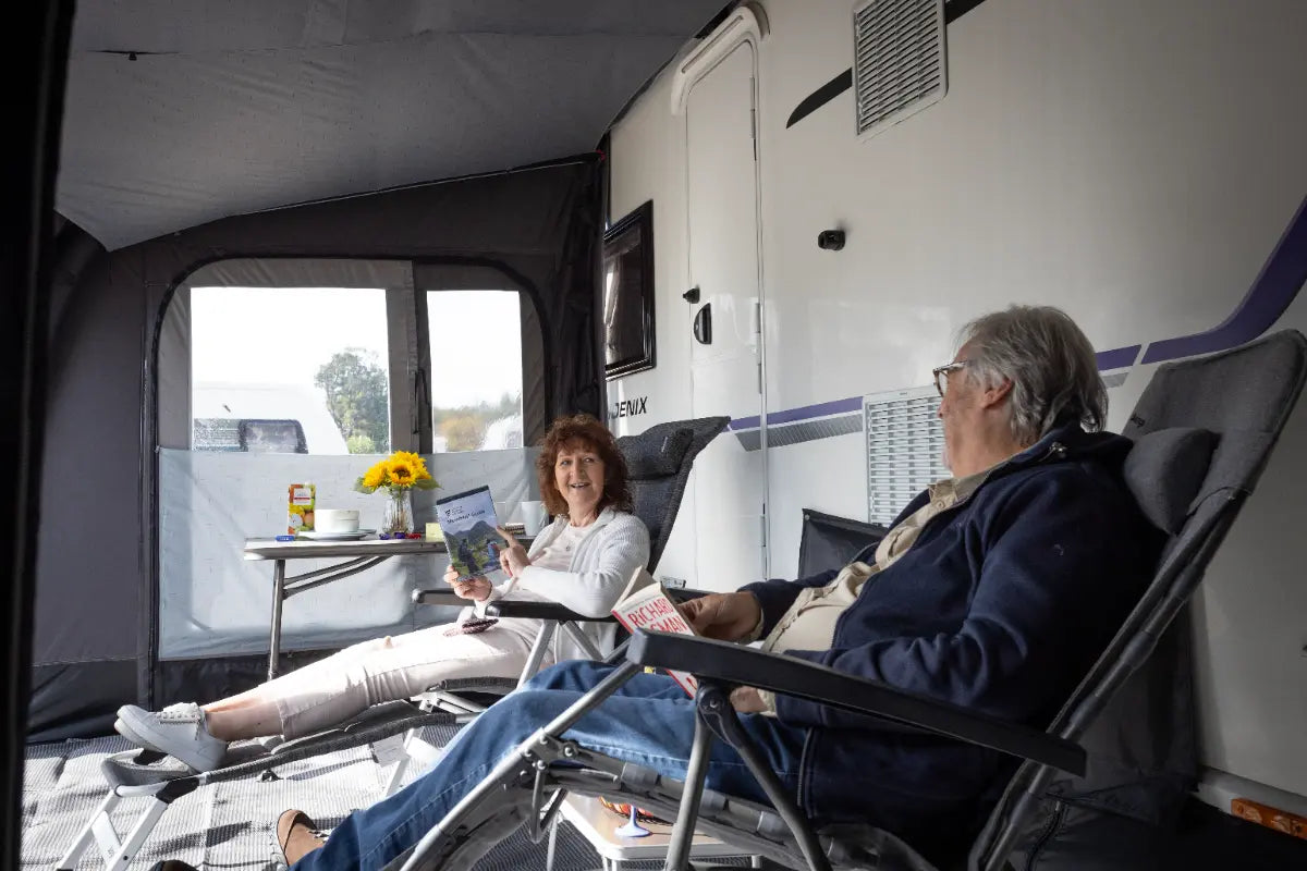 Two people relaxing inside the Vango Tuscany Pro Air 400 awning with a table and chairs.