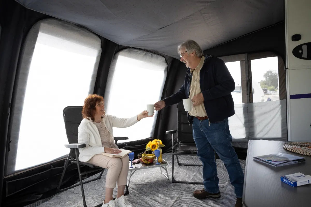 Two people inside the Vango Tuscany Pro Air 400 with large windows, one person handing a cup to the other.